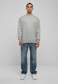 Sudadera gris con un cuello redondo y hombros caídos, combinada con jeans de mezclilla azul claro y zapatillas blancas. Diseño simple y casual.