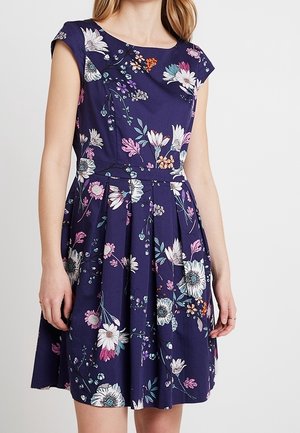 Une robe bleu marine à la longueur des genoux avec des manches capes, ornée d'un motif floral en rose, blanc et vert marine. Elle présente un corsage ajusté et une jupe plissée.