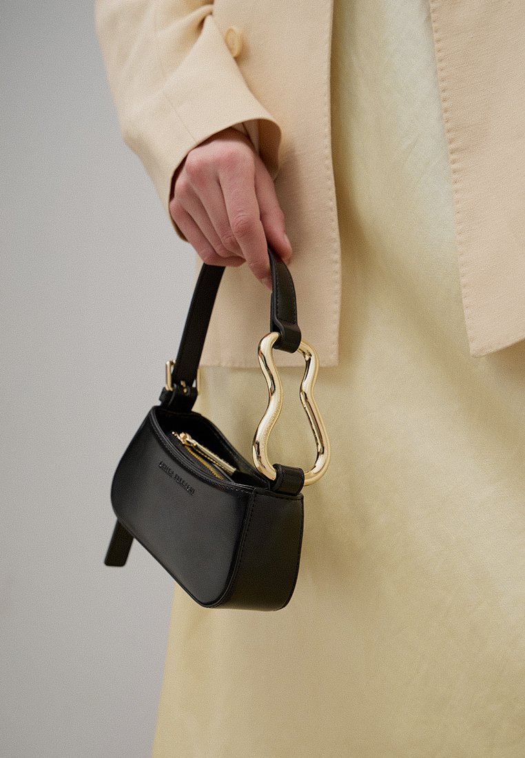 Schwarze Lederhandtasche mit einem geschwungenen Griff aus goldfarbenem Metall, mit einem Reißverschlussöffnung und einem strukturierten, rechteckigen Design.