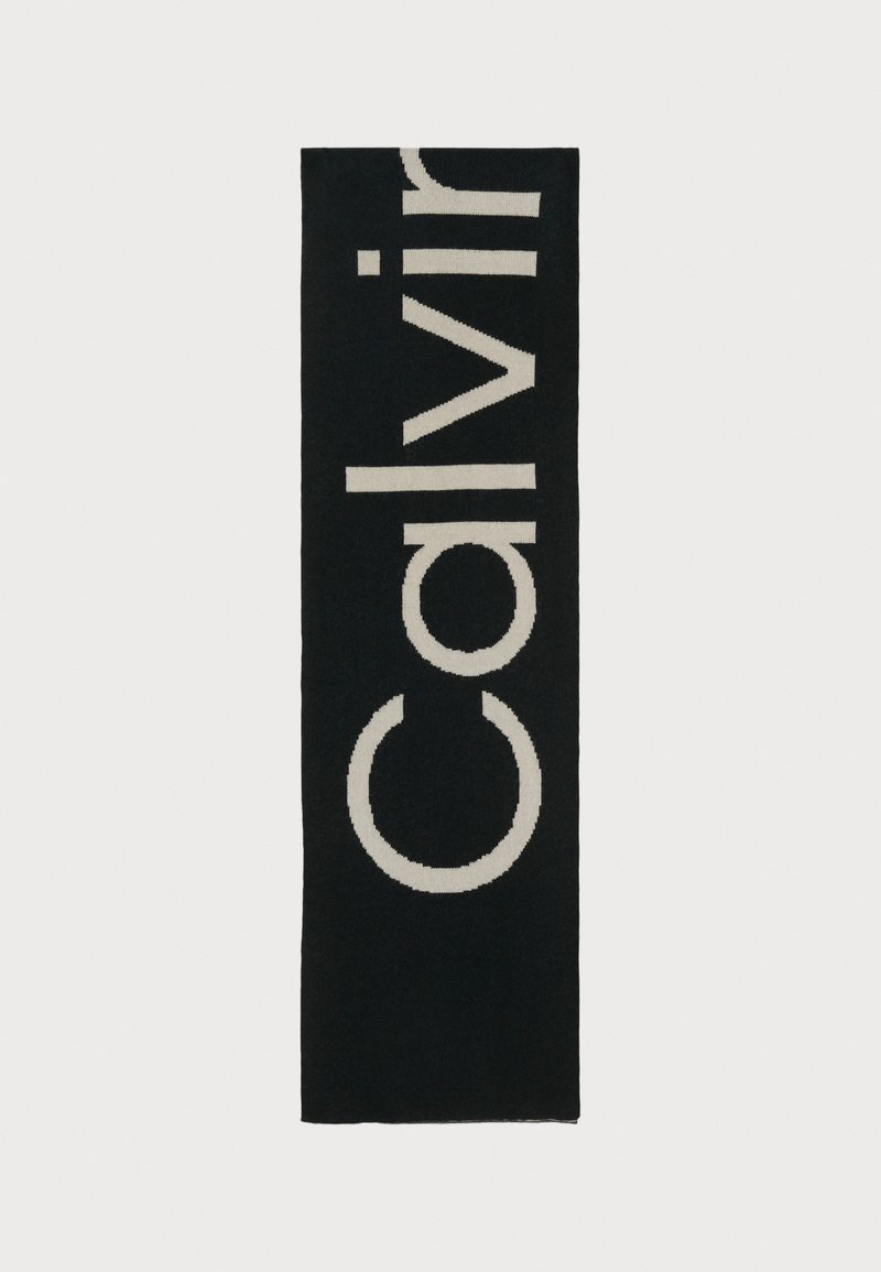 Svart bade matte med stor, kremfarget "Calvin"-tekst og sirkulært design i en kontrasterende farge. Laget av myk, teksturert stoff.