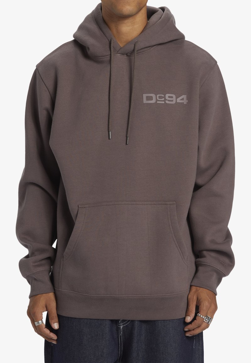 Grijze hoodie gemaakt van zachte stof, met een voorzak en een bedrukt logo "DC 94" op de linkerkant van de borst.