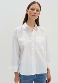 Camicia bianca in cotone con taschino sul petto, maniche ripiegate e vestibilità comoda. Texture morbida, design classico del colletto e orlo curvo.