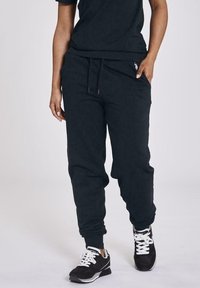 Pantaloni jogger neri realizzati in tessuto morbido, con vita elasticizzata, tasche laterali e polsini elasticizzati, abbinati a sneaker bianche e nere.