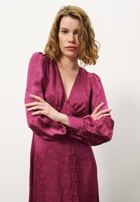 Robe à manches longues, décolletée en V profonde en satin bordeaux riche avec des accents de boutons, motif floral texturé et épaules froncées.