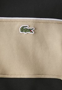 Chemise à manches courtes avec un corps noir et une bande horizontale beige, accentuée par un logo de crocodile vert brodé sur la bande.