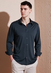 Houten lange mouwen knoopshirt in antraciet met een zachte textuur, gespreide kraag en opgerolde manchetten, met een gebogen zoom en contrasterende knopen.