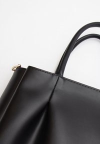Zwarte leren tote bag met twee handvatten, een gladde textuur, minimalistisch ontwerp en een goudkleurige accent aan de bovenrand.