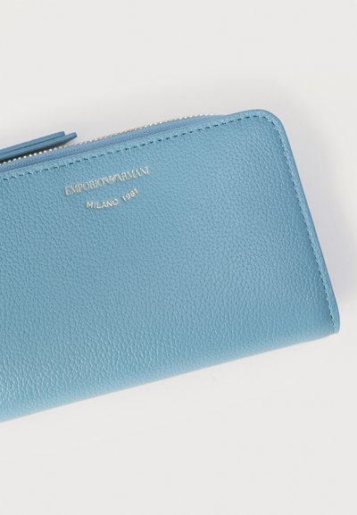 Φωτεινό γαλάζιο πορτοφόλι από δερμάτινη υφή με φερμουάρ που καλύπτει όλο το περίγραμμα, με χρυσό λογότυπο Emporio Armani και το κείμενο Milano 1981 στο κέντρο στην κορυφή.