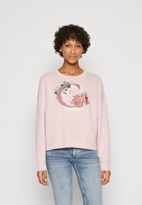 Sudadera de color rosa claro con cuello redondo y hombros caídos, que presenta bordados florales y la letra "G" en un detalle intrincado.