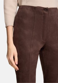 Bruine suède broek met een gladde textuur, voorzien van een sluiting met knopen aan de voorkant en rechte pijpen. Zijnaaddetails duidelijk zichtbaar van dichtbij.