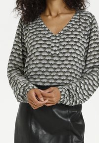 Langarmbluse aus grünem Stoff mit einem Fächer-Muster in Weiß, mit einem V-Ausschnitt und einem Knopfdetail unterhalb des Halses.