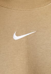 Tecido de sweatshirt bege com colarinho canelado. Apresenta um logo da Nike bordado em branco do lado esquerdo. Textura lisa, sem padrões.