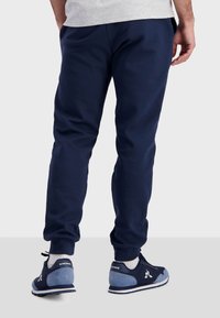 Donkerblauwe joggingsbroek met elastische boorden en een losse pasvorm, gemaakt van zacht materiaal. Gepaard met donkerblauwe en blauwe sportschoenen.