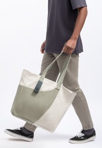 Borsa in tela per la spesa in verde e crema, con manici corti, design curvo e un'etichetta grigia con logo delle forbici.