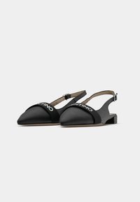 Zapatos slingback negros con punta puntiaguda, hechos de un material liso. Cuentan con una correa elástica con la marca "Valentino" y un tacón bajo tipo bloque.