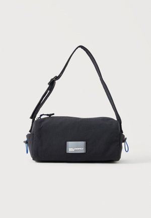 Sort cylindrisk skuldertaske med justerbar rem, blå lynlåstræk og frontlabel med teksten "KARL LAGERFELD JEANS" mod en hvid baggrund.