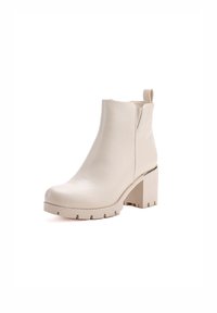Botas de tobillo beige hechas de cuero suave, con tacón cuadrado, punta redondeada y una lengüeta en la parte posterior. Suela texturizada para mayor agarre.