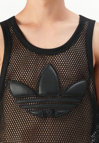 Cămașă fără mâneci din plasă neagră, cu o guler cu textură ribbed și un logo proeminent din piele neagră cu un design în formă de trei frunze, situat în centrul său.