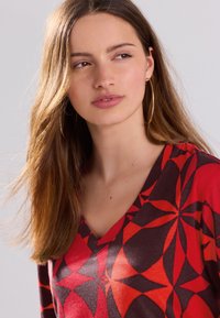 Red and black patterned top with a V-neck design, made of soft fabric. Features floral geometric shapes and a relaxed fit.