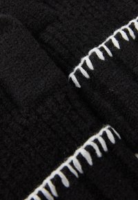 Tissu noir tricoté avec un motif texturé, comportant des accents de fil blanc le long d'un bord. Matière douce et chaude.