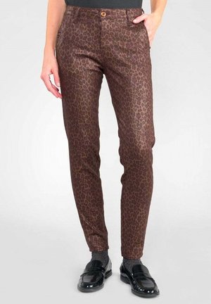 Schmal geschnittene braune Hose mit dezentem Leopardenmuster, brauner Knopfverschluss, kombiniert mit schwarzen Slippern und grauen Socken.