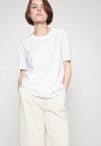 White short-sleeve t-shirt made of smooth cotton, relaxed fit, round neckline, paired with light beige wide-leg trousers.