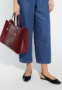 Sac en cuir bordeaux avec deux poignées et des accents dorés, associé à un jean large bleu foncé et des chaussures à talons slingback en vernis noir.