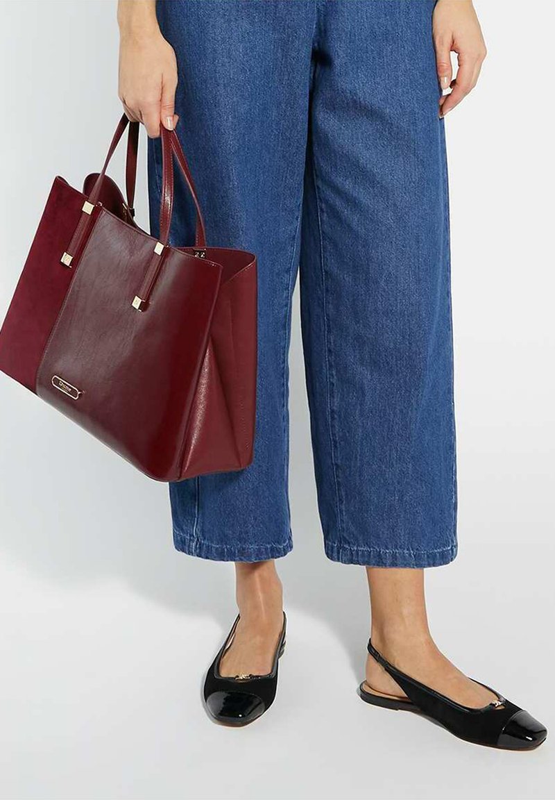 Sac en cuir bordeaux avec deux poignées et des accents dorés, associé à un jean large bleu foncé et des chaussures à talons slingback en vernis noir.