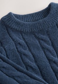 Pull en maille torsadée bleu marine avec un col ras du cou côtelé et une texture duveteuse, présentant un motif de brins torsadés sur tout le tissu.