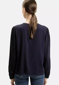 Granatowa koszula z długim rękawem, z marszczonymi ramionami i okrągłym dekoltem. Tkanina wydaje się miękka z teksturowanym wykończeniem. Casualowy fason z bocznymi rozcięciami.