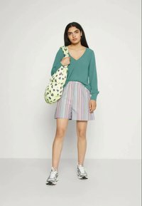 Sweater turquesa de decote em V, calções às riscas em cores pastel e uma bolsa verde com padrão de folhas. Ténis cinza com detalhes metálicos.