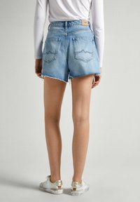 Shorts de mezclilla en azul claro, de tiro alto con dobladillo deshilachado. Presenta dos bolsillos traseros con costura en forma de ola y una etiqueta de cuero con la marca.