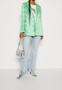 Blazer a rayas verde cebra, camiseta gráfica blanca, jeans acampanados de un azul claro, bolso de mano curvado plateado, botas de tobillo puntiagudas plateadas.