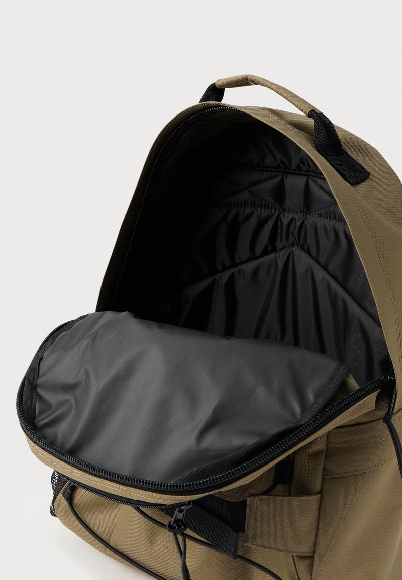 Offener khakifarbener Rucksack mit schwarzem gepolstertem Innenfach und Reißverschlussklappe, inklusive Griff und Details zur Fronttasche.