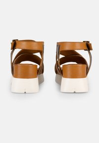 Sandales en cuir marron avec un design à large sangle, bride de cheville réglable et un talon bloc blanc. Texture lisse et style minimaliste.