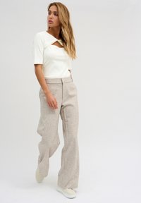 White ribbed top with a cutout, paired with beige wide-leg trousers. Model wears light sneakers. Simple, modern design with soft textures.