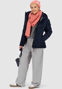 Giacca puffer blu navy, maglione grigio, pantaloni grigio chiaro, sciarpa e berretto lavorati a maglia rosa. Gli accessori includono una borsa piccola e sneakers bianche.