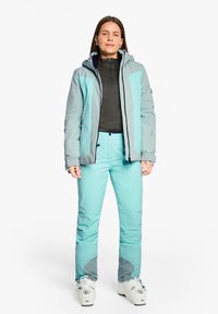 Skiausrüstung mit einer hellblauen und grauen Jacke mit Kapuze, schwarzem Midlayer und türkisen Skihosen. Strukturiertes Material mit Akzenten.