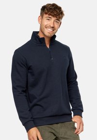 Marineblå pullover sweatshirt med lynlås krave, ribbede manchetter og talje. Har et lille logo på brystet. Blødt, tekstureret stof.