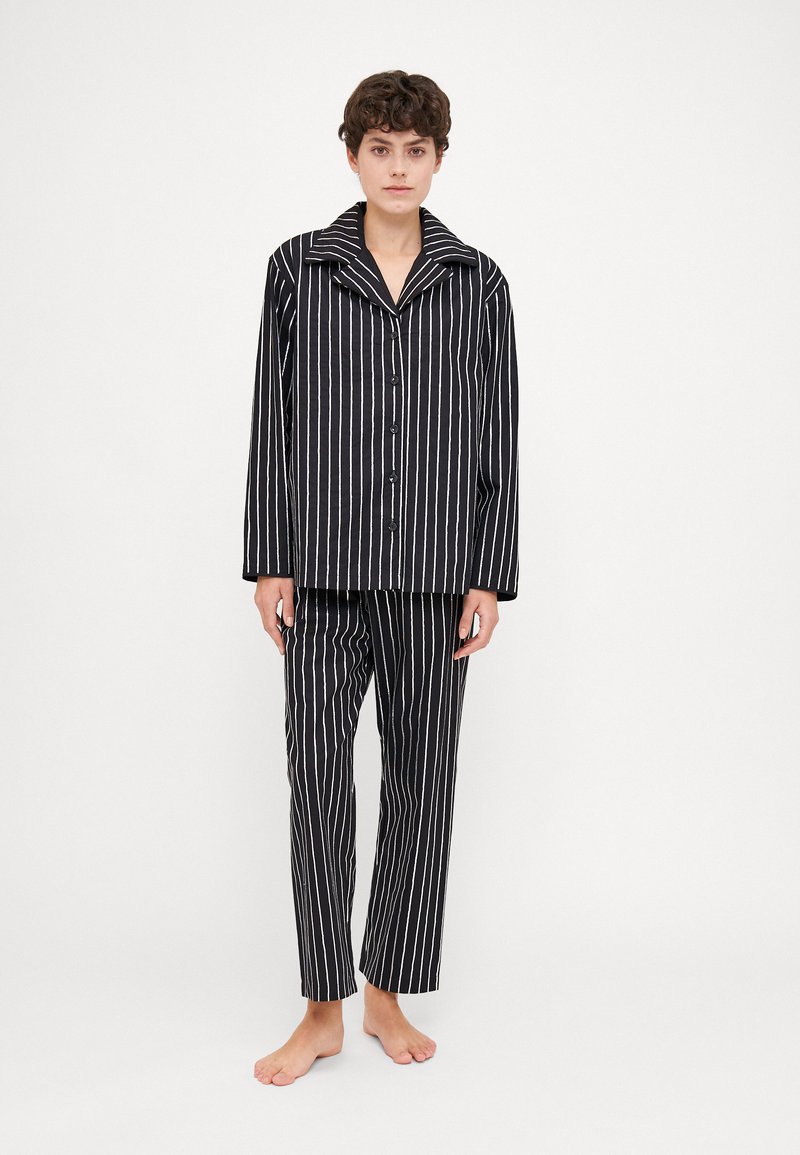 Pajama set dengan garis hitam dan putih yang menampilkan kemeja berlengan panjang dengan kerah dan celana lurus yang serasi, terbuat dari kain lembut.