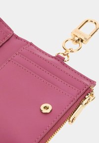 Portefeuille en simili cuir rose avec quincaillerie dorée, doté d'une fermeture à glissière, de détails de couture et d'un clip détachable.