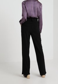 Svarta högmidjade byxor med vid benpassform och subtila sidoindelningar, tillsammans med en lila randig långärmad blus.