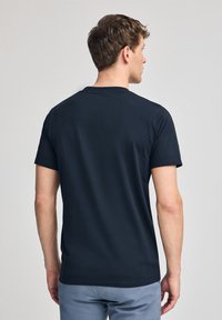 Marinblå t-shirt i mjuk bomull, med rundad hals och korta ärmar. Baksidan visar en jämn, konsekvent textur utan mönster.