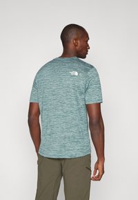 Lühikeste varrukatega, ümaralt lõigatud T-särk tekstuurse teali värvi kangast, millel on valge logo selja ülaosas. Sobitatud oliiviroheline lühikesed püksid.