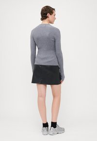 Grå ribbestrikket genser med lange ermer, kombinert med et svart mini skjørt i kunstlær. Modellen har på seg grå sneakers og svarte anklestøvler.