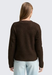 Brauner, gerippter Strickpullover mit langen Ärmeln, Rundhalsausschnitt und lässiger Passform, der aus strukturiertem Material gefertigt ist und einen leicht verkürzten Saum hat.