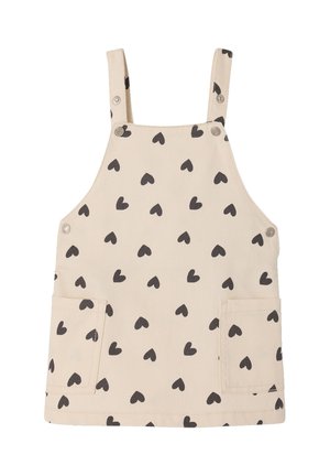 Beiger Kinderlatzkleid mit schwarzem Herzmuster, zwei Fronttaschen und verstellbaren Schulterriemen mit Metallknöpfen.