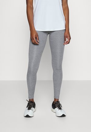 Leggings grises hechos de una tela elástica, con una textura suave y un diseño ajustado. Combinados con zapatillas deportivas en blanco y negro.