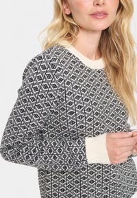 Kreemja ja musta geomeetrilise mustriga kootud sviiter. Omab ribatud kaelust ja varrukaotsi, pakkudes tekstuurset ja sooja väljanägemist.