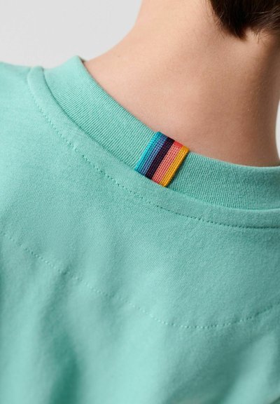 Close-up af en hals iført en mintgrøn skjorte med ribbet krave og lille multifarvet stofmærke bagpå.